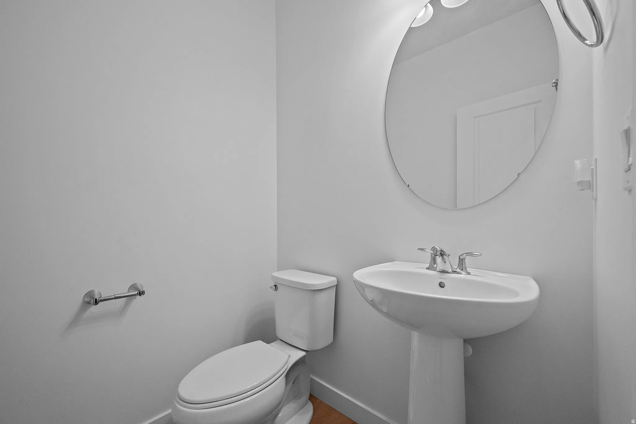 Pedestal sink with chrome faucet, oval frameless mirror, and overhead vanity lighting