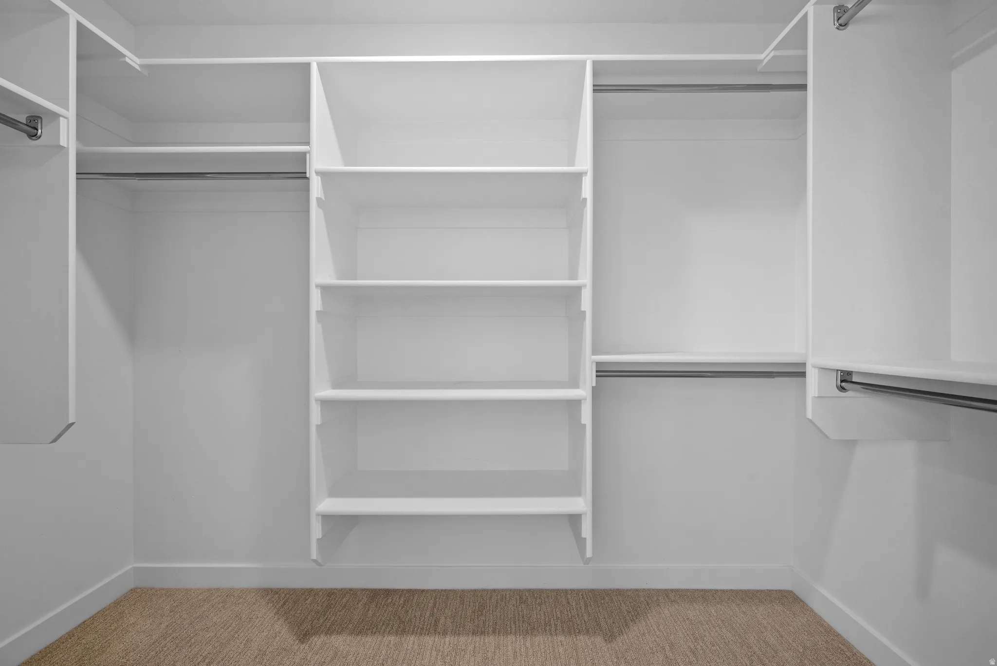 Walk-in closet featuring white built-in shelving, multiple hanging rods, white walls, white baseboards, and tan carpeting