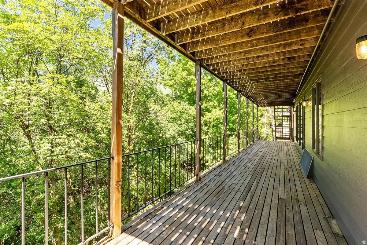 Expansive wood-finish deck with black metal railings, a covered ceiling, and exterior wall lighting
