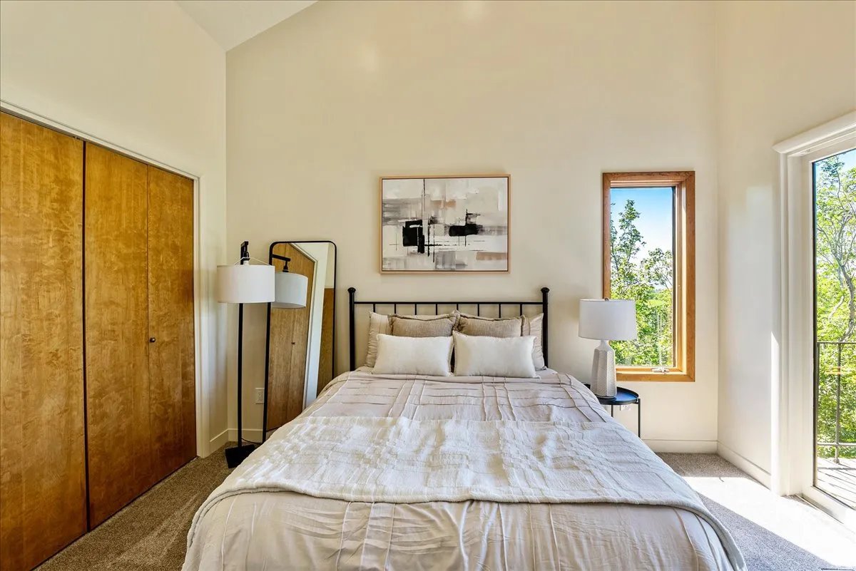 Vaulted ceiling room featuring light-toned walls, wood-finish bi-fold closet doors, a tall window with wood trim, and a glass-paneled door opening to an exterior space