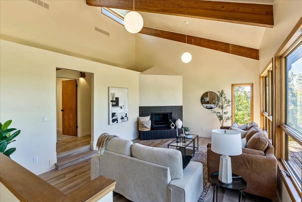 Vaulted living area featuring exposed wood beams, a skylight, and wood-finish flooring