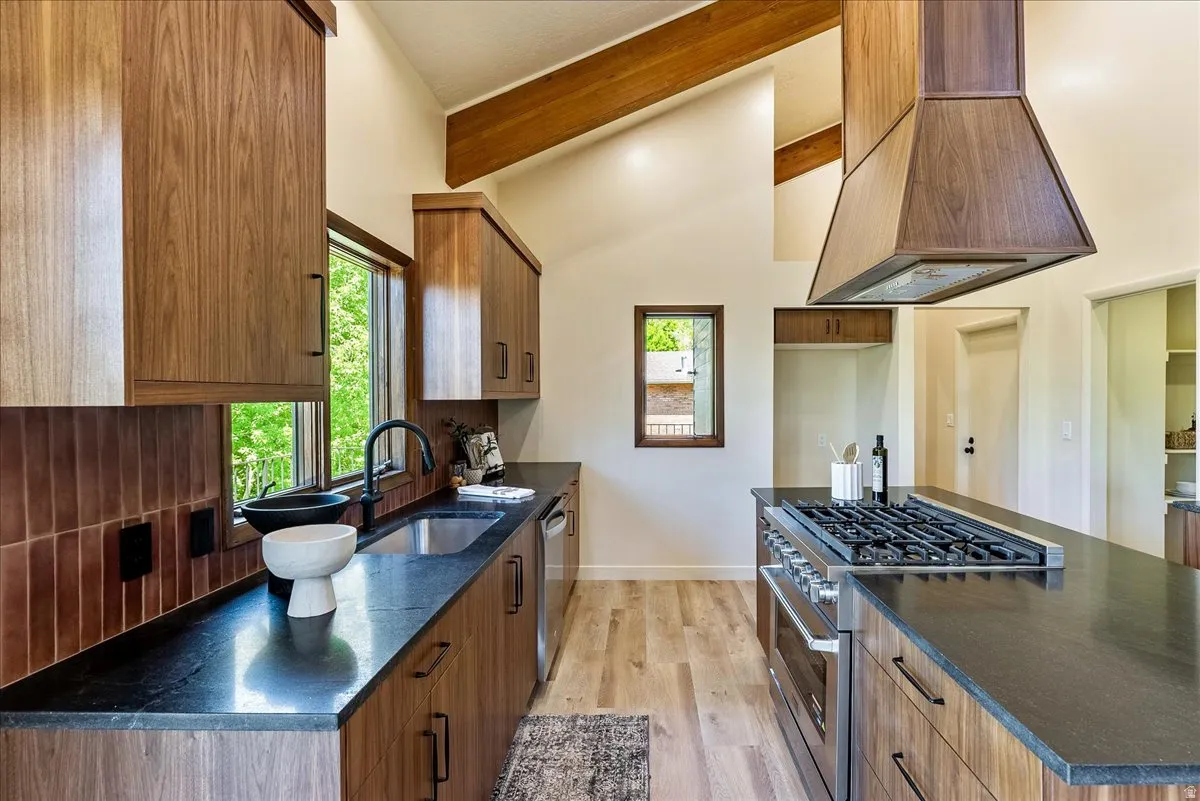 Contemporary kitchen showcasing wood-finish cabinetry, dark countertops, a stainless steel range with a built-in oven, and a matching wood-finish range hood