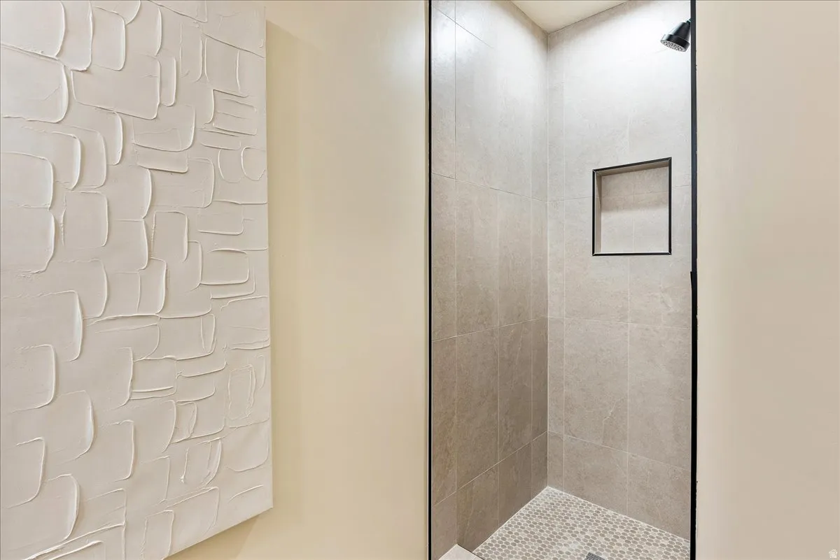 Shower enclosure featuring light-toned large-format wall tiles and a contrasting mosaic tile floor