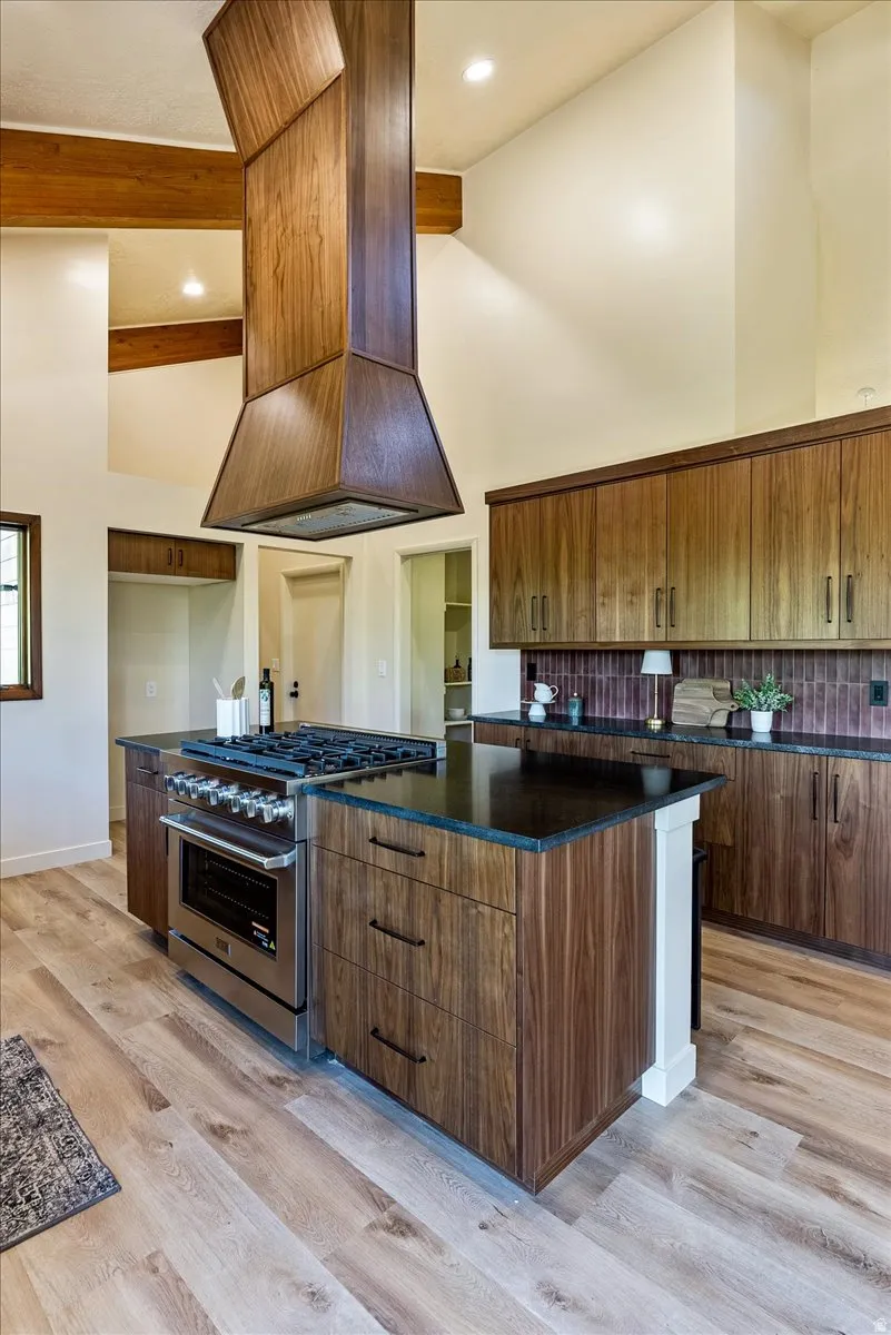 Open-concept kitchen with a custom wood-paneled range hood, wood-finish flooring, and dark stone countertops