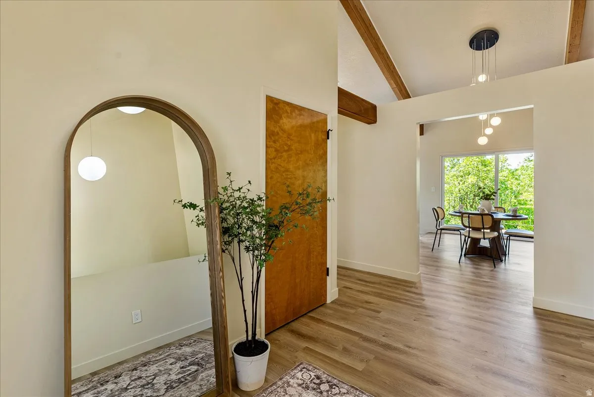 Bright interior space featuring wood-finish flooring, exposed ceiling beams, and a natural wood door