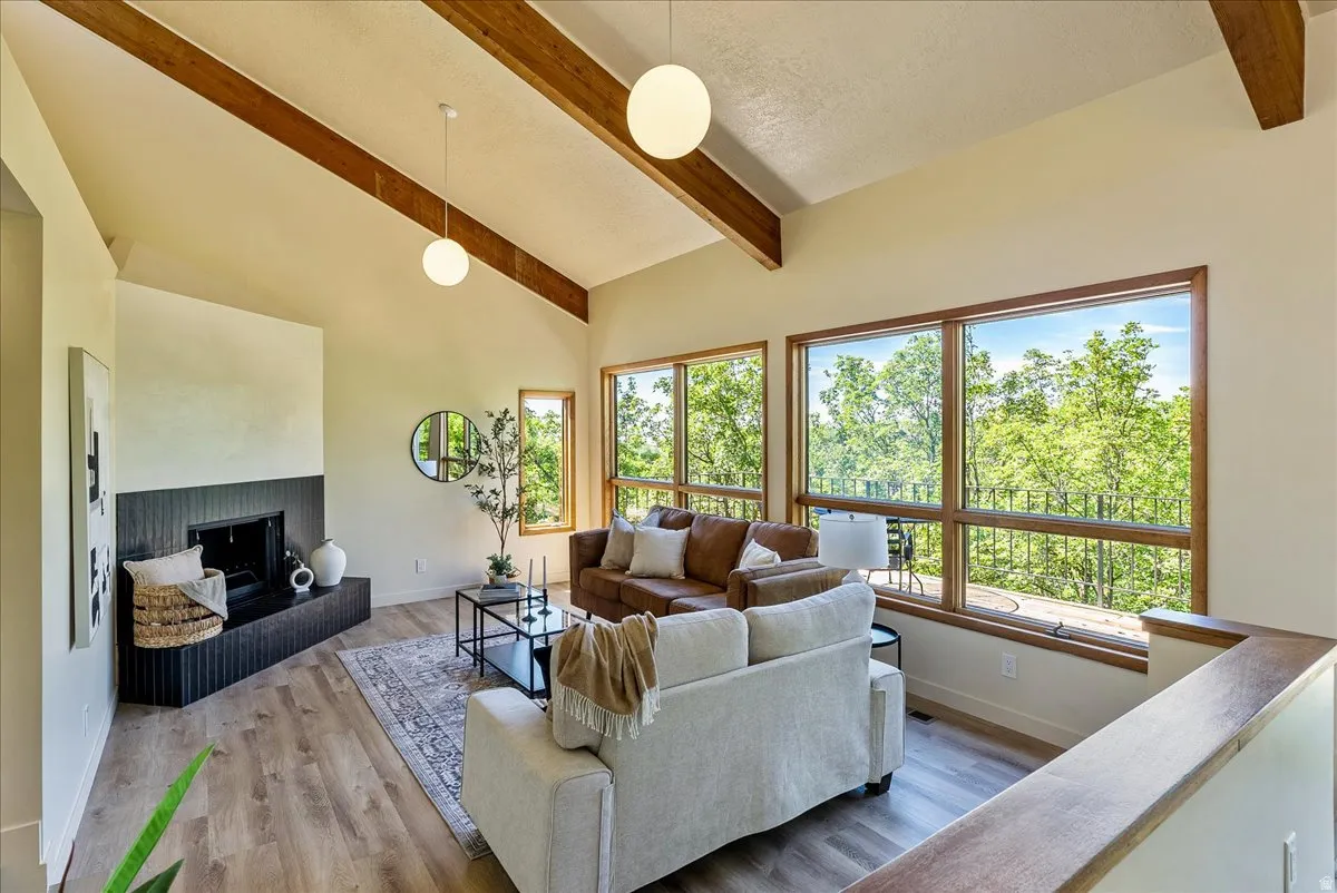 Living area featuring exposed wood beams, vaulted ceilings, expansive windows, a textured fireplace surround, and wood-finish flooring