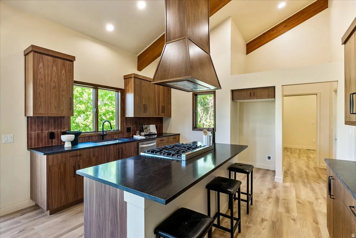 Modern kitchen featuring vaulted ceilings with exposed beams, recessed lighting, and wood-finish cabinetry