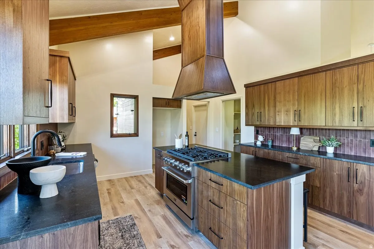 Kitchen featuring vaulted ceilings with exposed wood beams, wood-finish flooring, a central island with a gas range, dark countertops, and extensive wood cabinetry