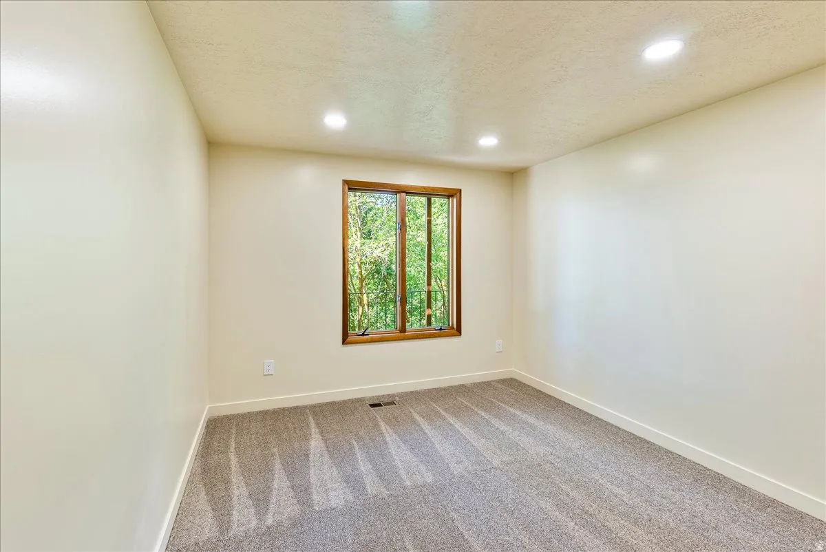 Recessed lighting illuminates this room featuring light-toned walls and gray carpeting