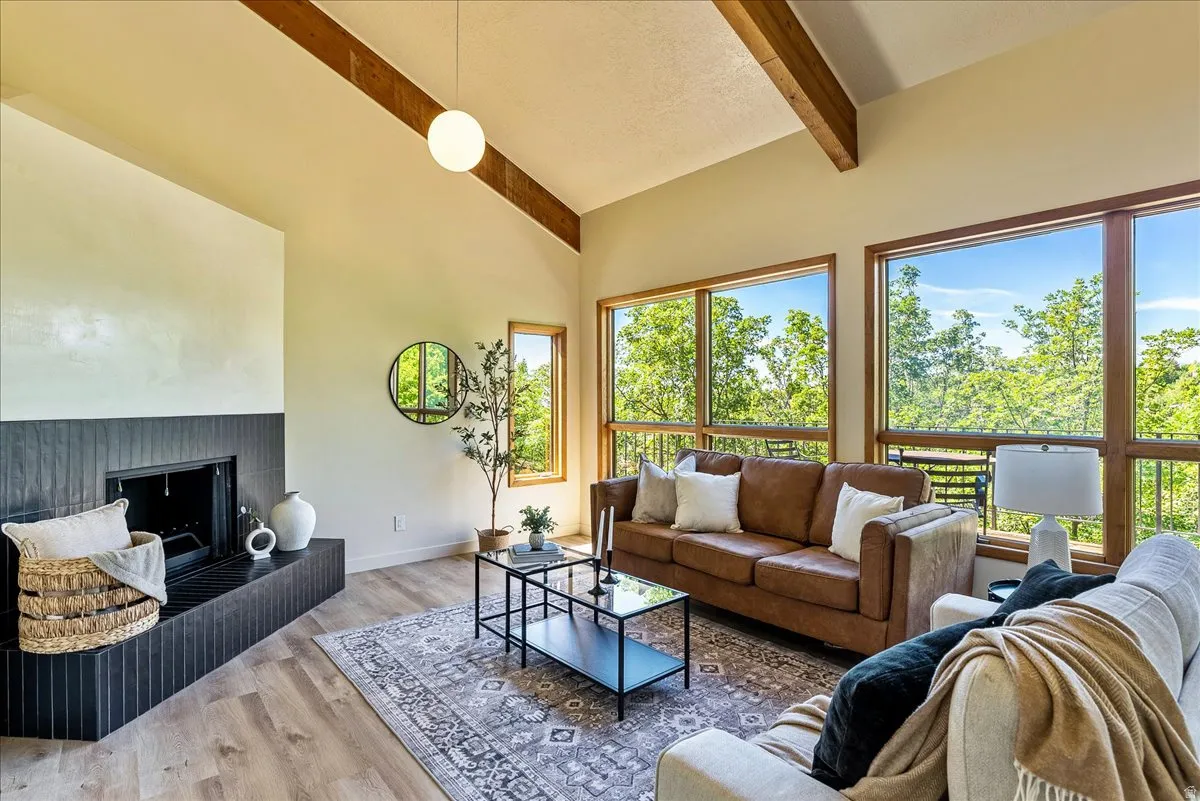 Vaulted ceiling with exposed wood beams, wood-finish flooring, and a modern fireplace with a dark tile surround