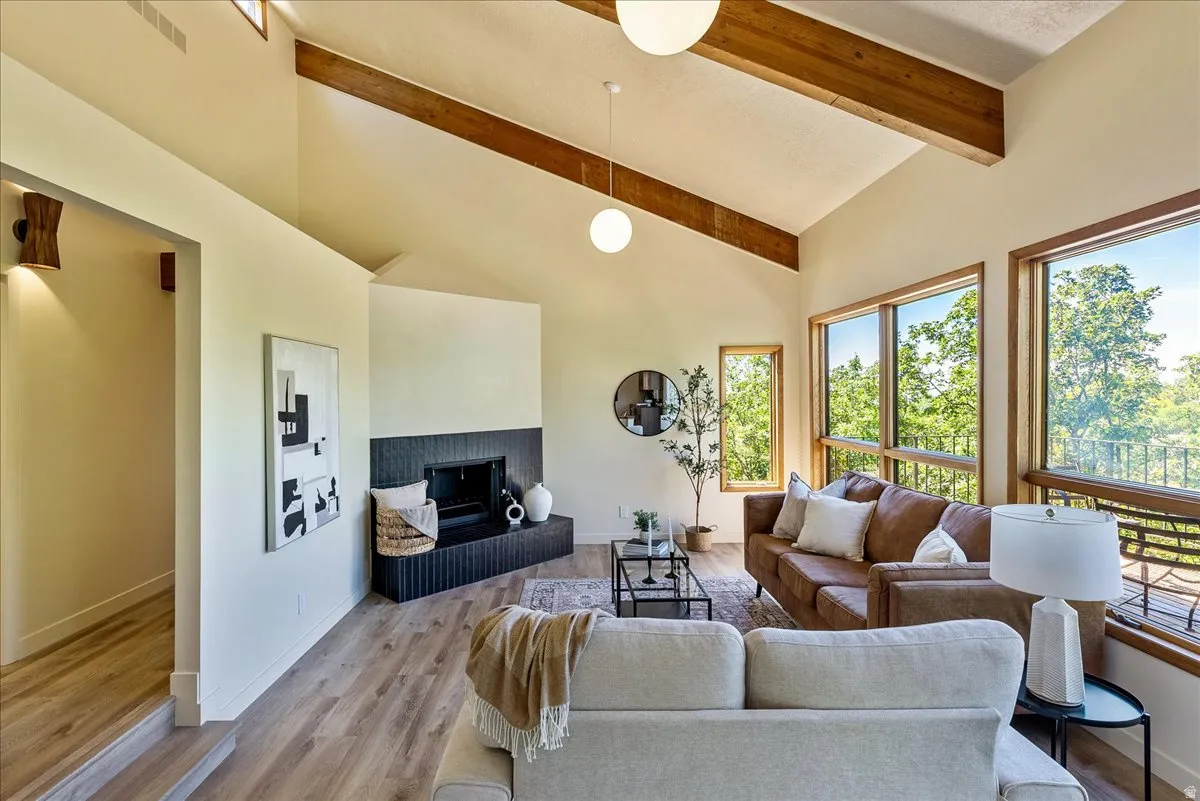 Vaulted ceilings featuring exposed wood beams, a modern fireplace with a dark fluted hearth, and wood-finish flooring