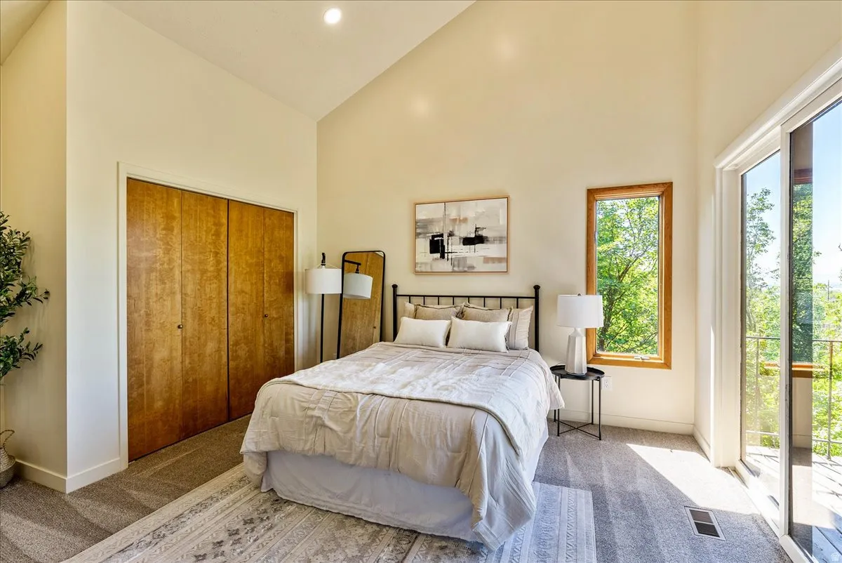 Vaulted ceilings define this space, featuring wood-finish bi-fold closet doors, a single-pane window with wood trim, and a glass sliding door opening to an exterior balcony