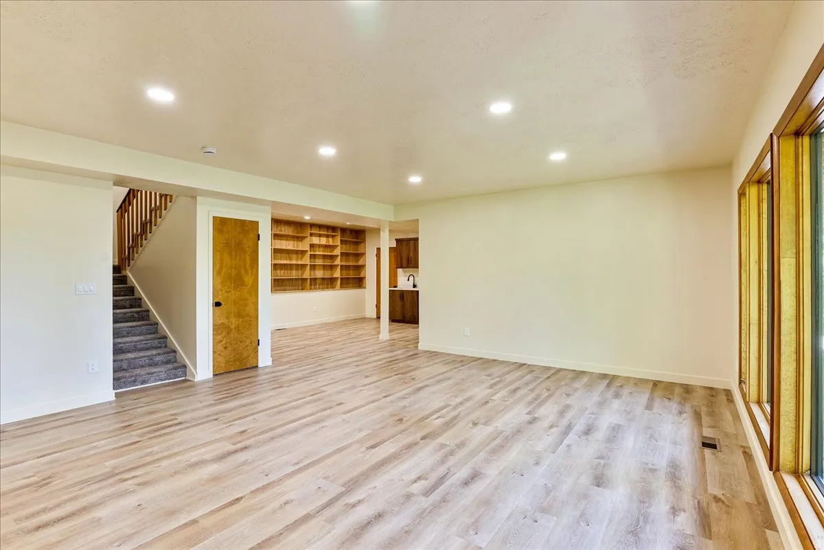 Spacious open-concept room featuring light wood-finish flooring, recessed lighting, and a prominent window bank with natural wood trim