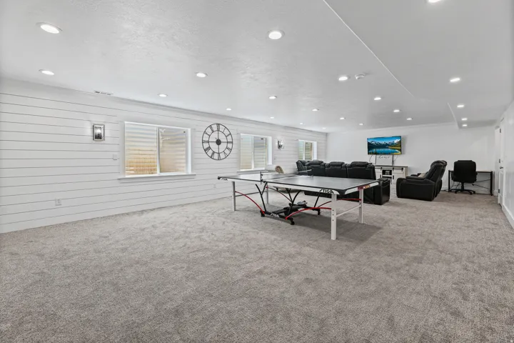 Spacious recreation room featuring light gray carpeting and white shiplap accent walls