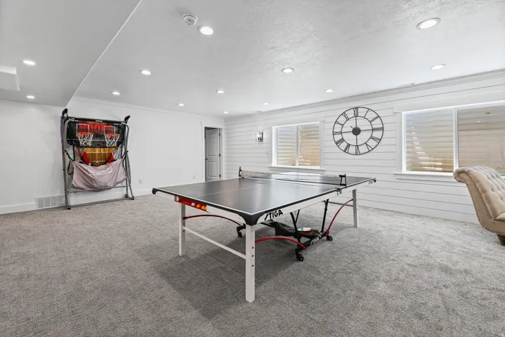 Spacious finished room featuring light gray carpeting, recessed lighting, and white shiplap accent wall with two egress windows