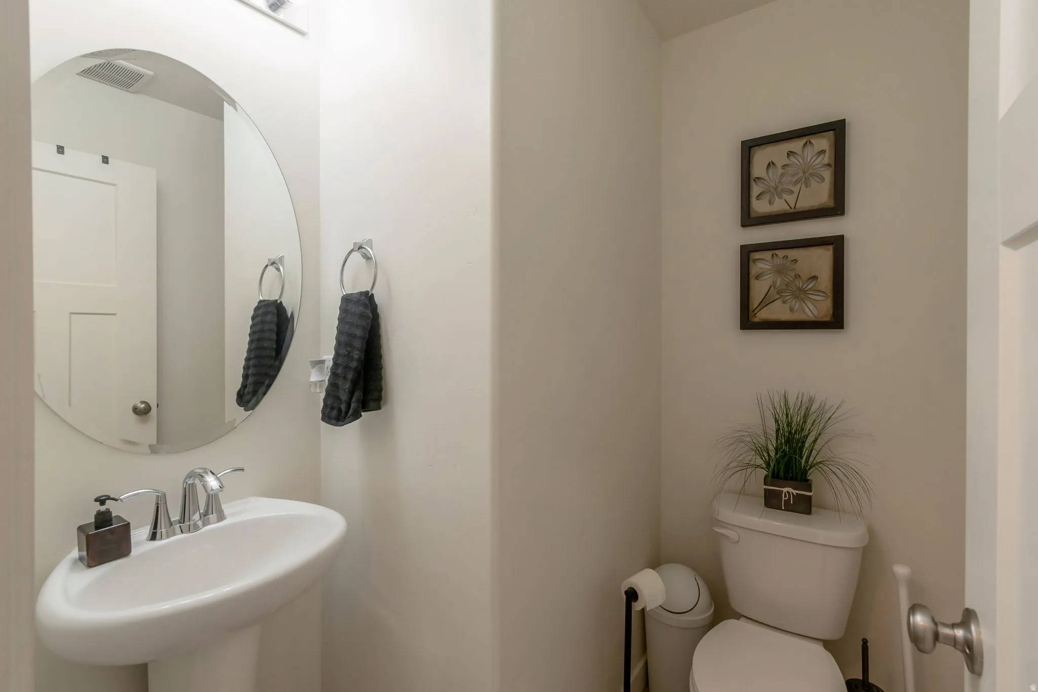 Pedestal sink with chrome fixtures and an oval mirror