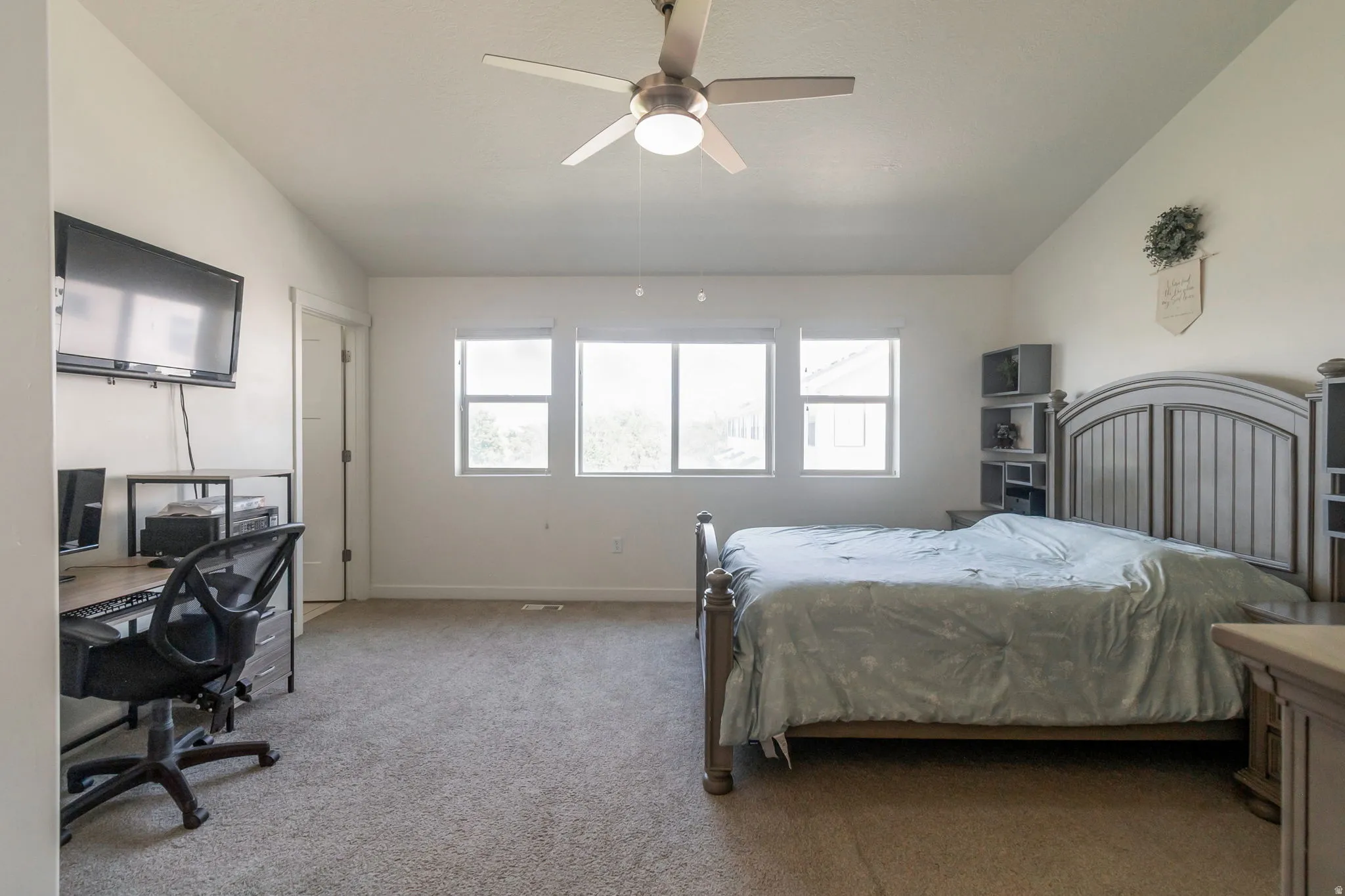 Spacious room featuring neutral carpeting, a ceiling fan with integrated lighting, and a wall of three windows