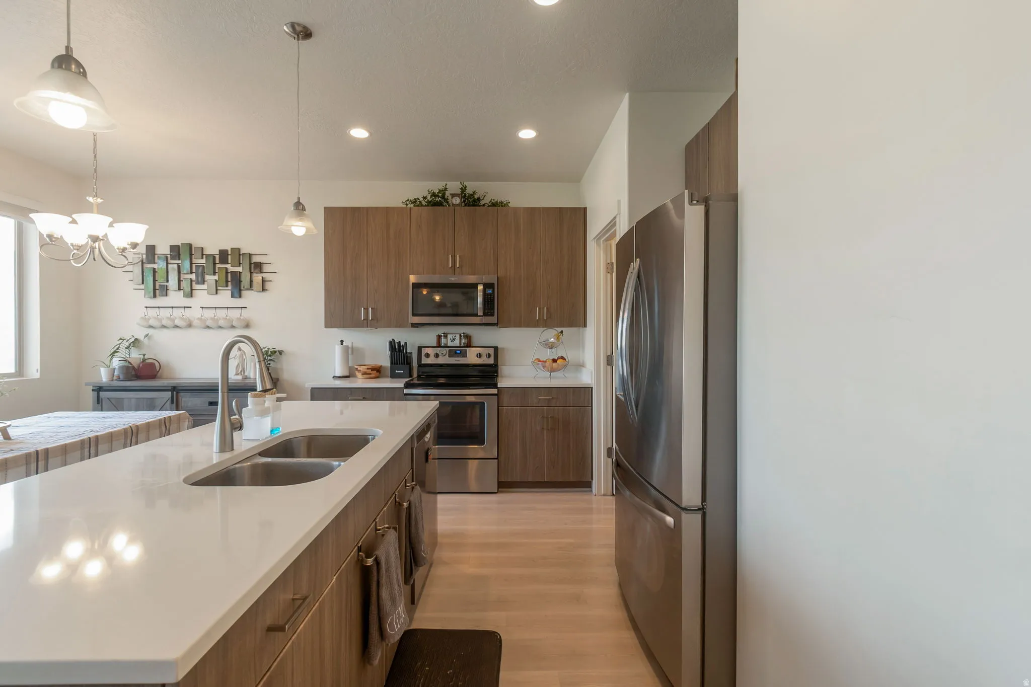 Kitchen featuring a double basin sink with a gooseneck faucet, light wood-finish cabinetry, stainless steel appliances, and light-toned countertops