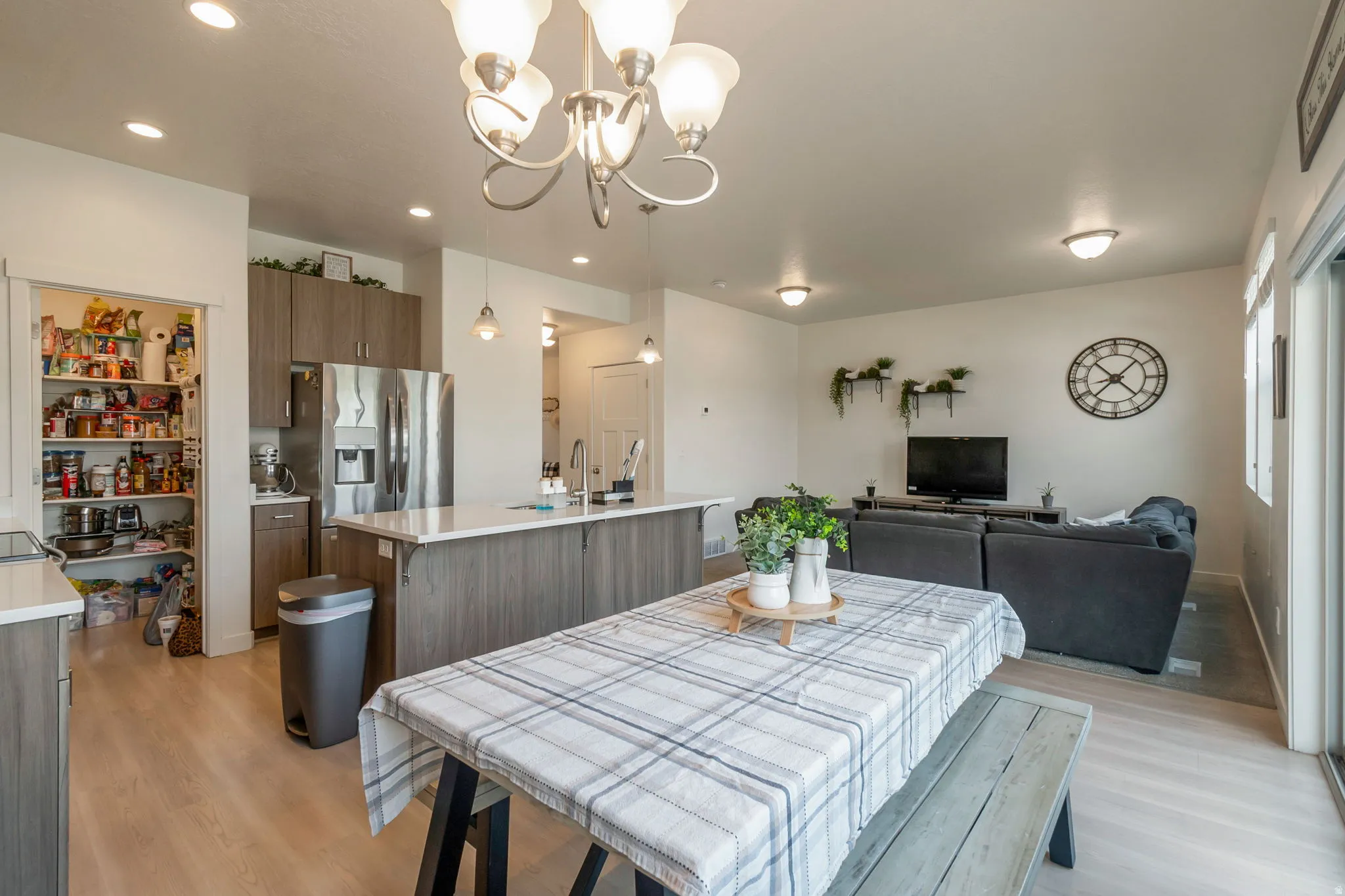 Open-concept living space featuring wood-finish flooring, a kitchen island with a light-toned countertop, stainless steel appliances, a pantry, and recessed lighting