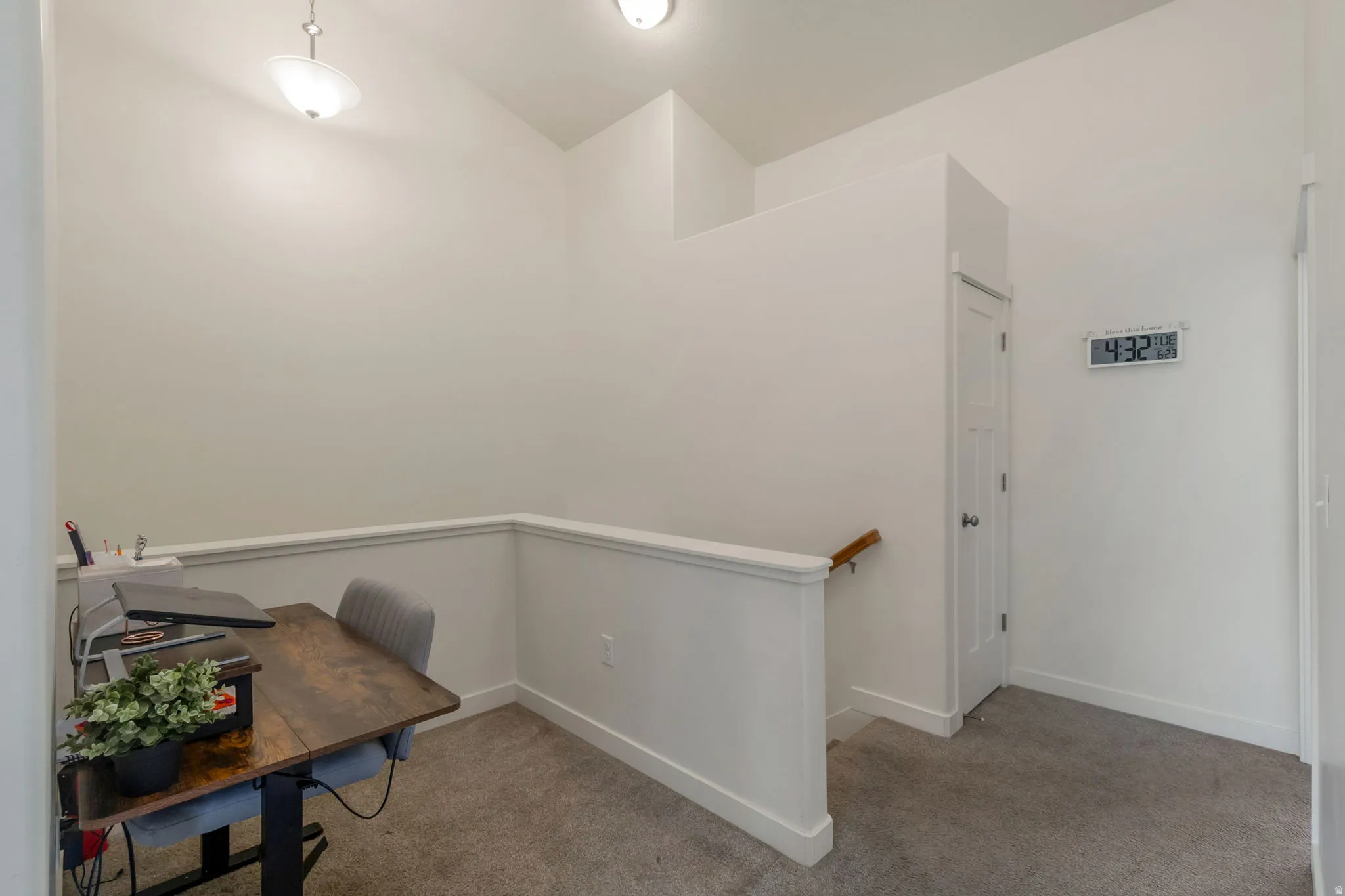 Carpeted landing featuring a built-in railing, neutral wall finishes, a white paneled door, and overhead lighting fixtures