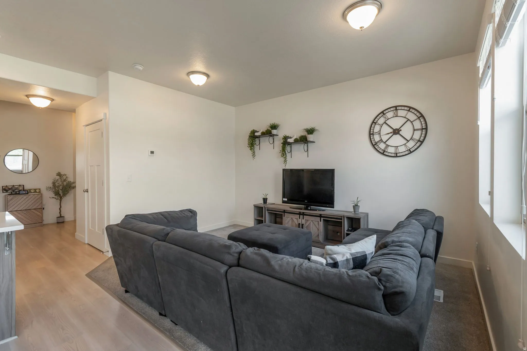 Open-concept living space featuring light wood-finish flooring, recessed ceiling lighting, abundant natural light from multiple windows, and a built-in media console with storage