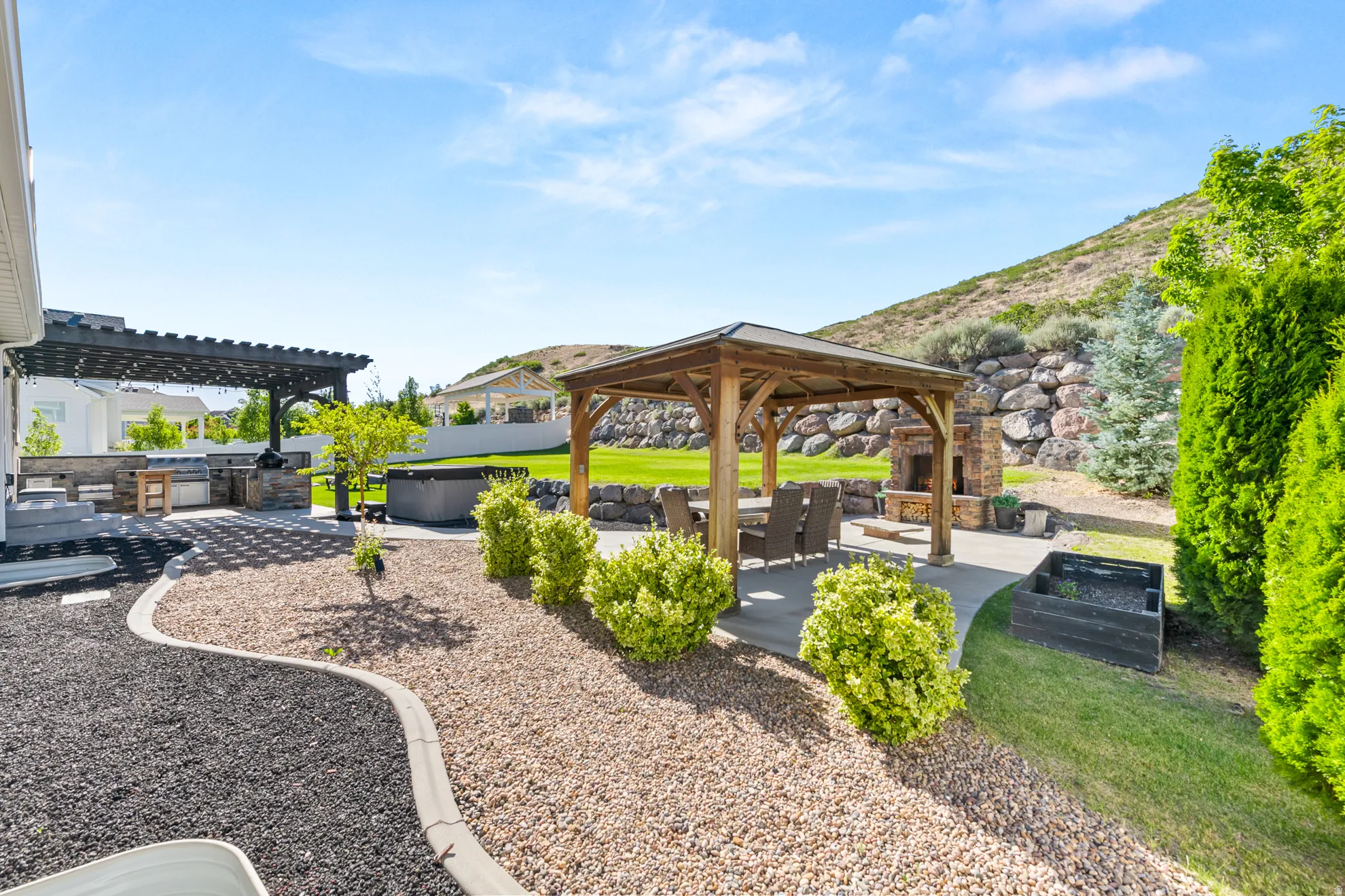 Expansive backyard featuring a stone fireplace, wood gazebo, and built-in outdoor kitchen with pergola