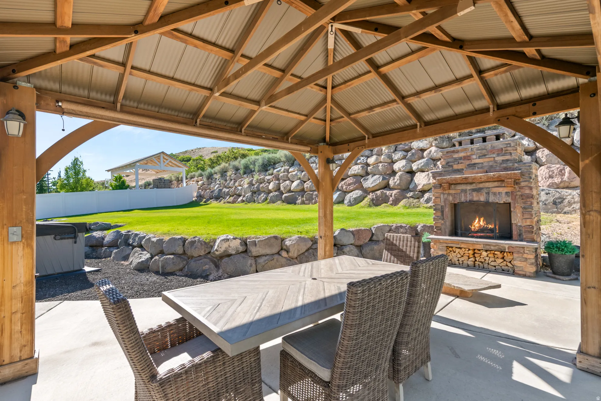 Covered patio featuring a wood-frame gazebo with a corrugated metal roof, al stone fireplace, and an expansive lawn