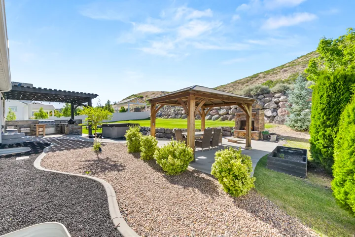 Expansive backyard featuring a stone fireplace, wood gazebo, and built-in outdoor kitchen with pergola
