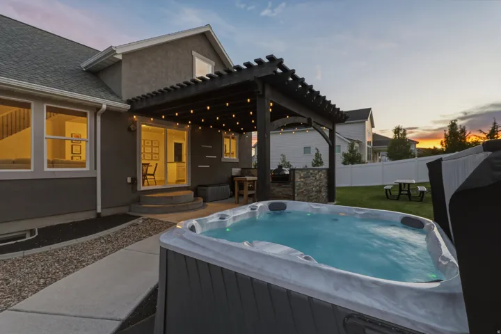 Backyard spa with concrete patio, gravel border, and a dark wood pergola