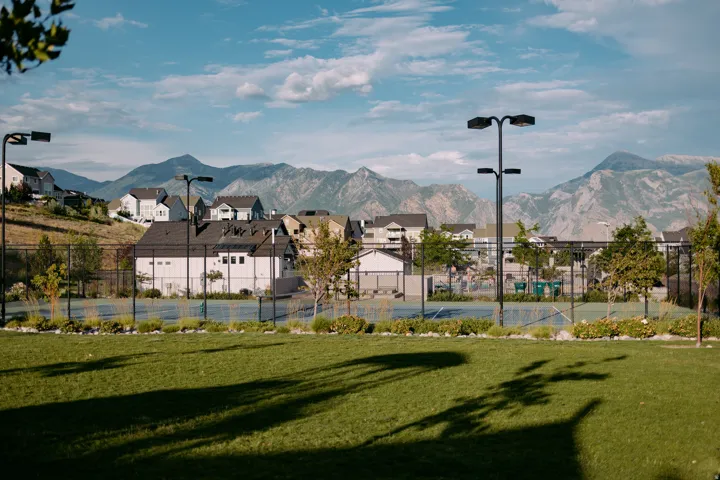 Community tennis courts with perimeter fencing and integrated lighting, framed by manicured green space and mature landscaping