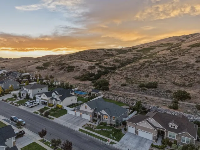 Residential neighborhood with a mountain backdrop, featuring a multi-level home with a two-car garage and a stone and siding exterior