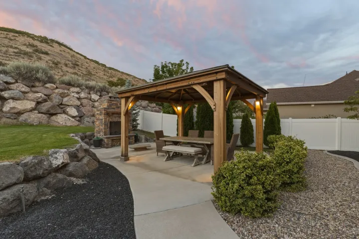 Outdoor entertaining space with a wood-frame gazebo, stone fireplace, and paved patio