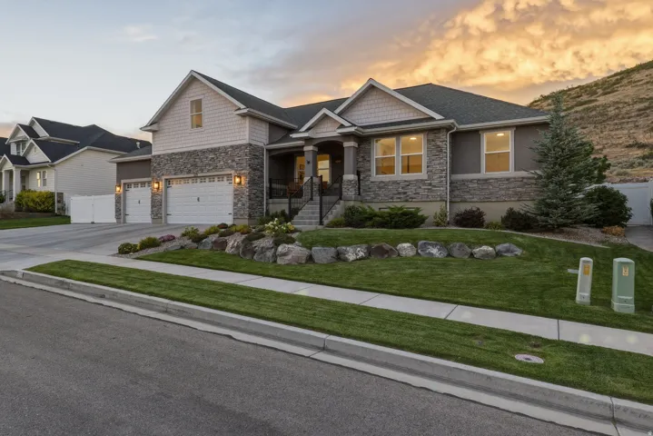 Two-story residence featuring stone and siding exterior, two-car garage, established front landscaping, and a concrete driveway