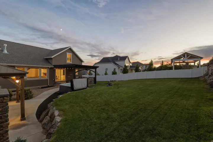 Expansive backyard with a manicured lawn, a large hot tub, a covered patio, a separate gazebo, and a privacy fence