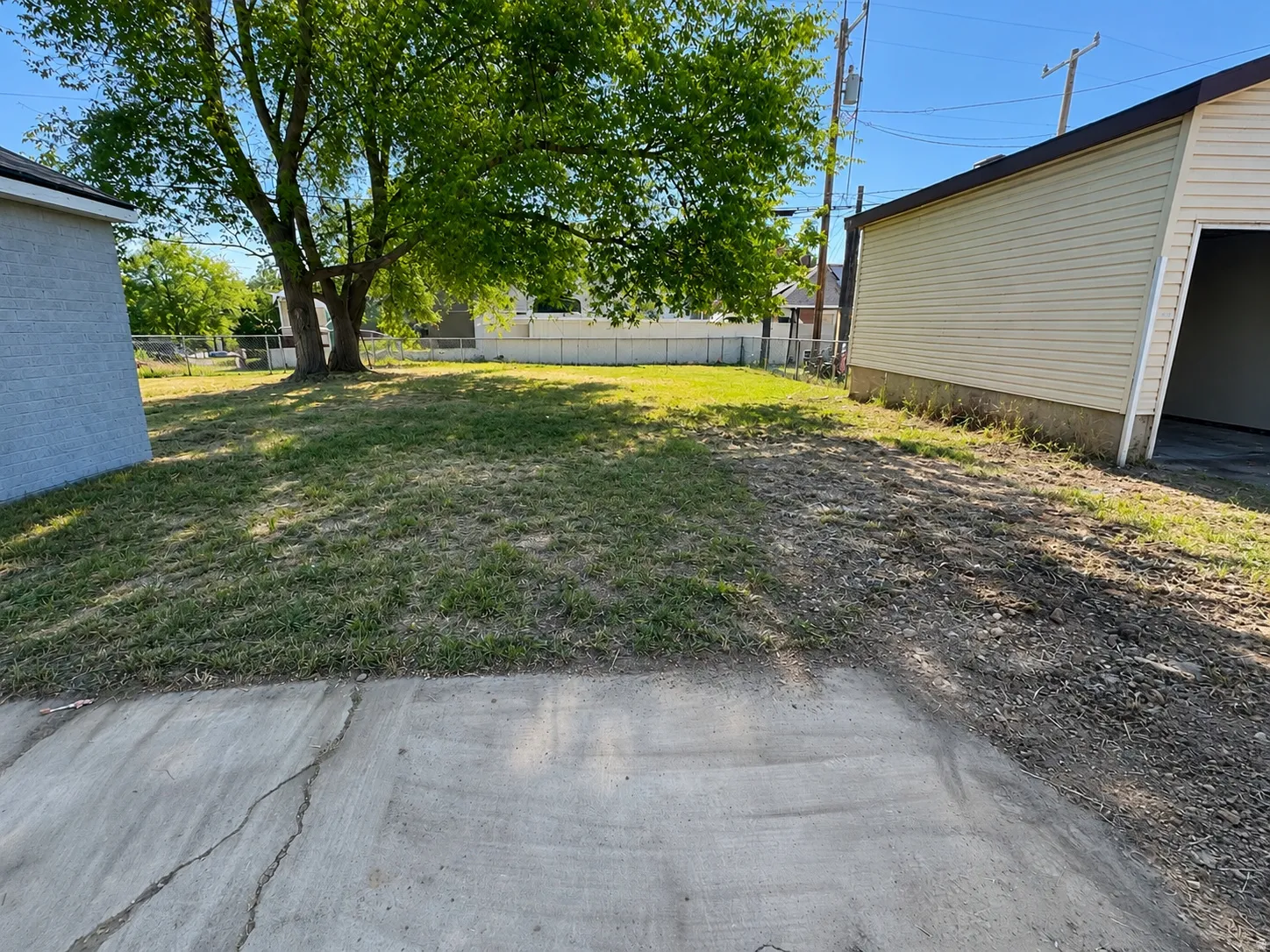 Expansive yard space featuring a mature tree, concrete pad, and a detached garage with horizontal siding