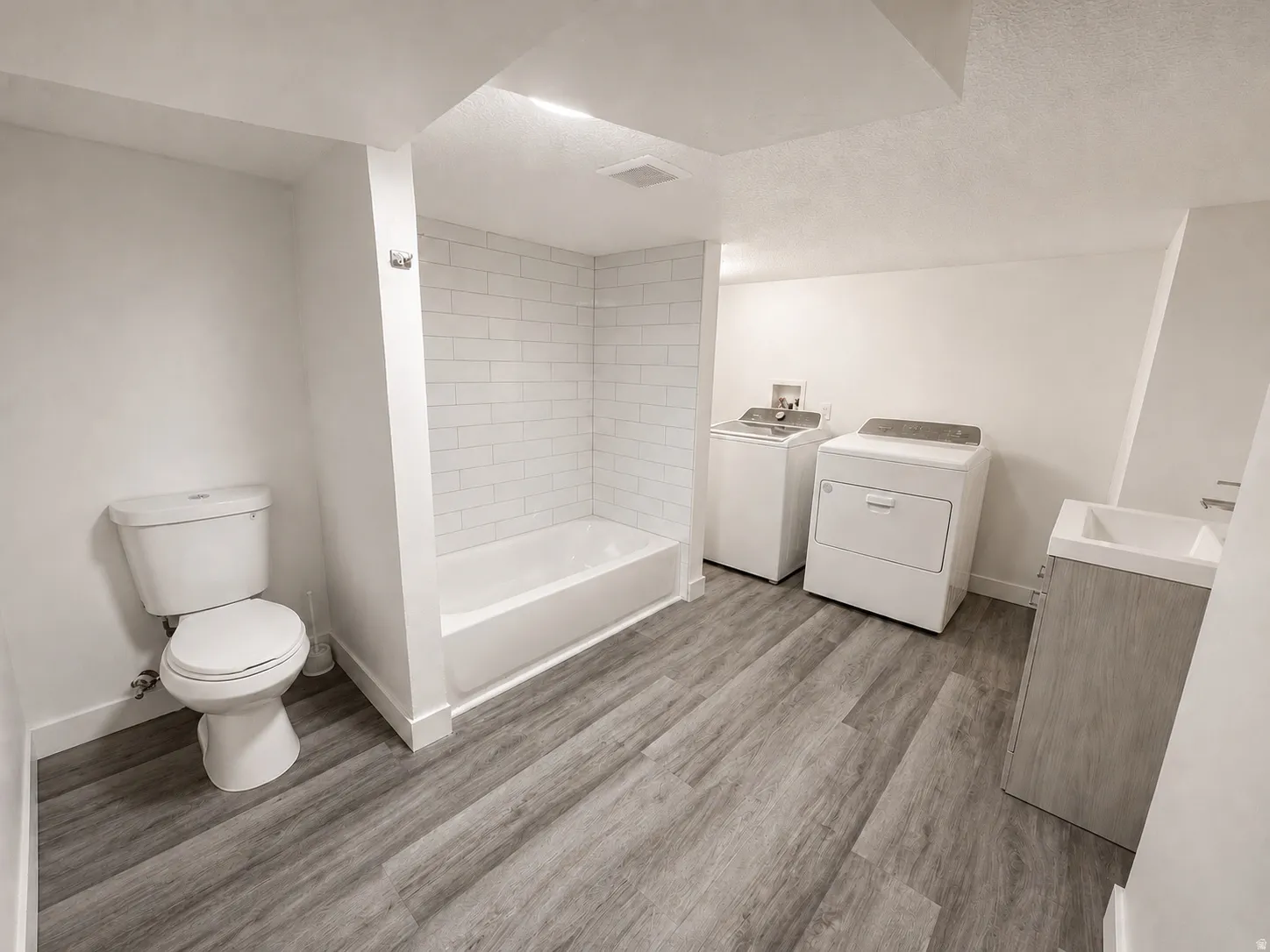 Bathroom featuring a white toilet, white bathtub with subway tile surround, and wood-finish flooring