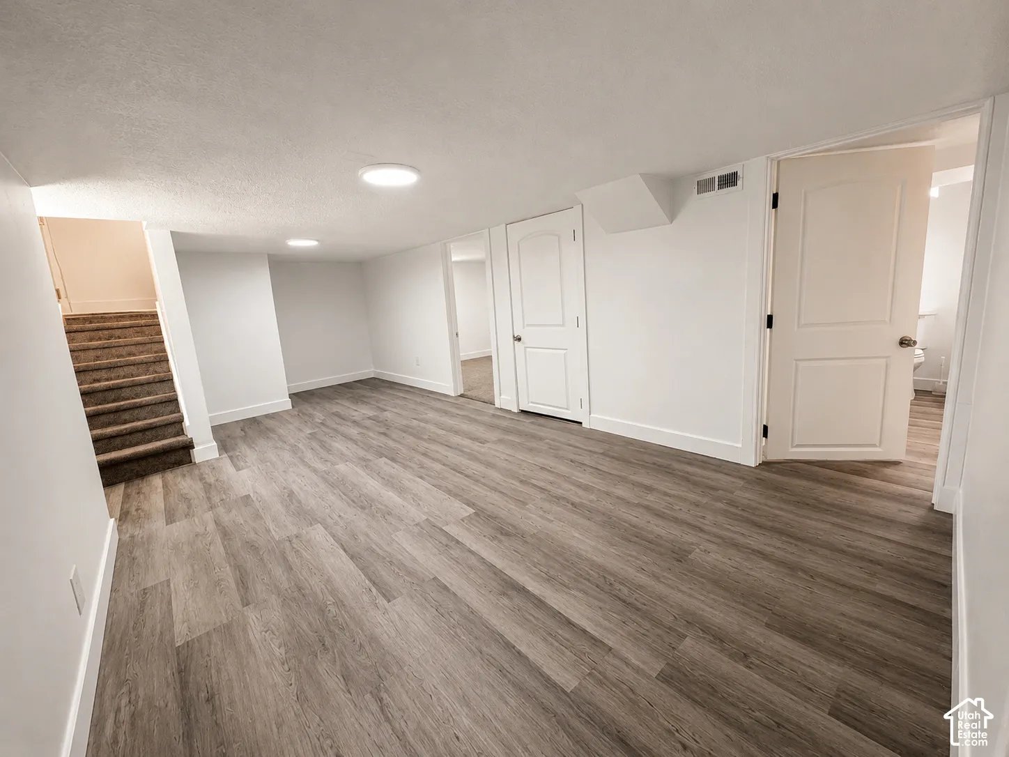 Spacious room featuring wood-finish flooring, white walls with matching baseboards, and bright ceiling lighting