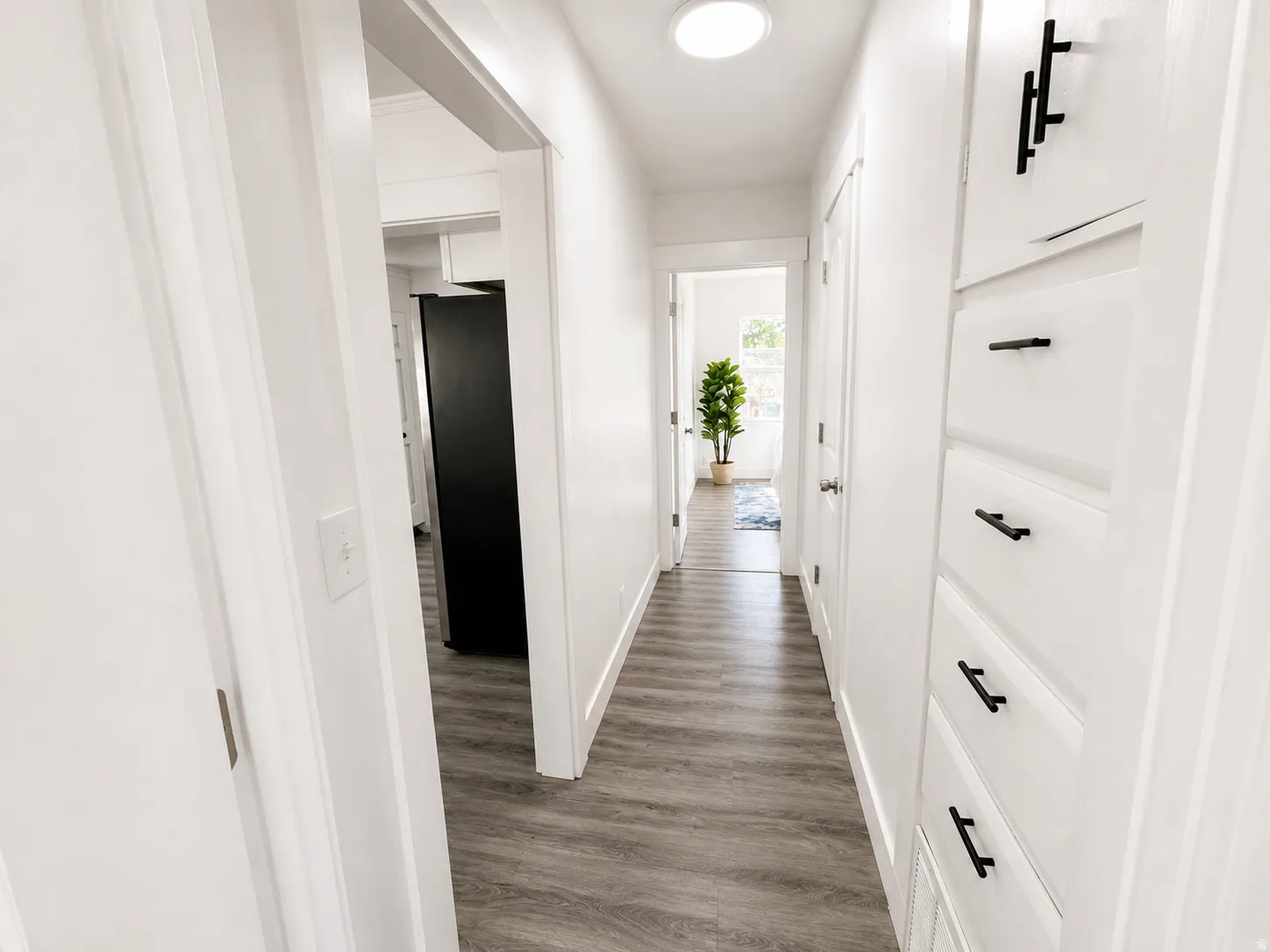 Hallway featuring wood-finish flooring, recessed lighting, white built-in cabinetry with matte black hardware, and crisp white walls