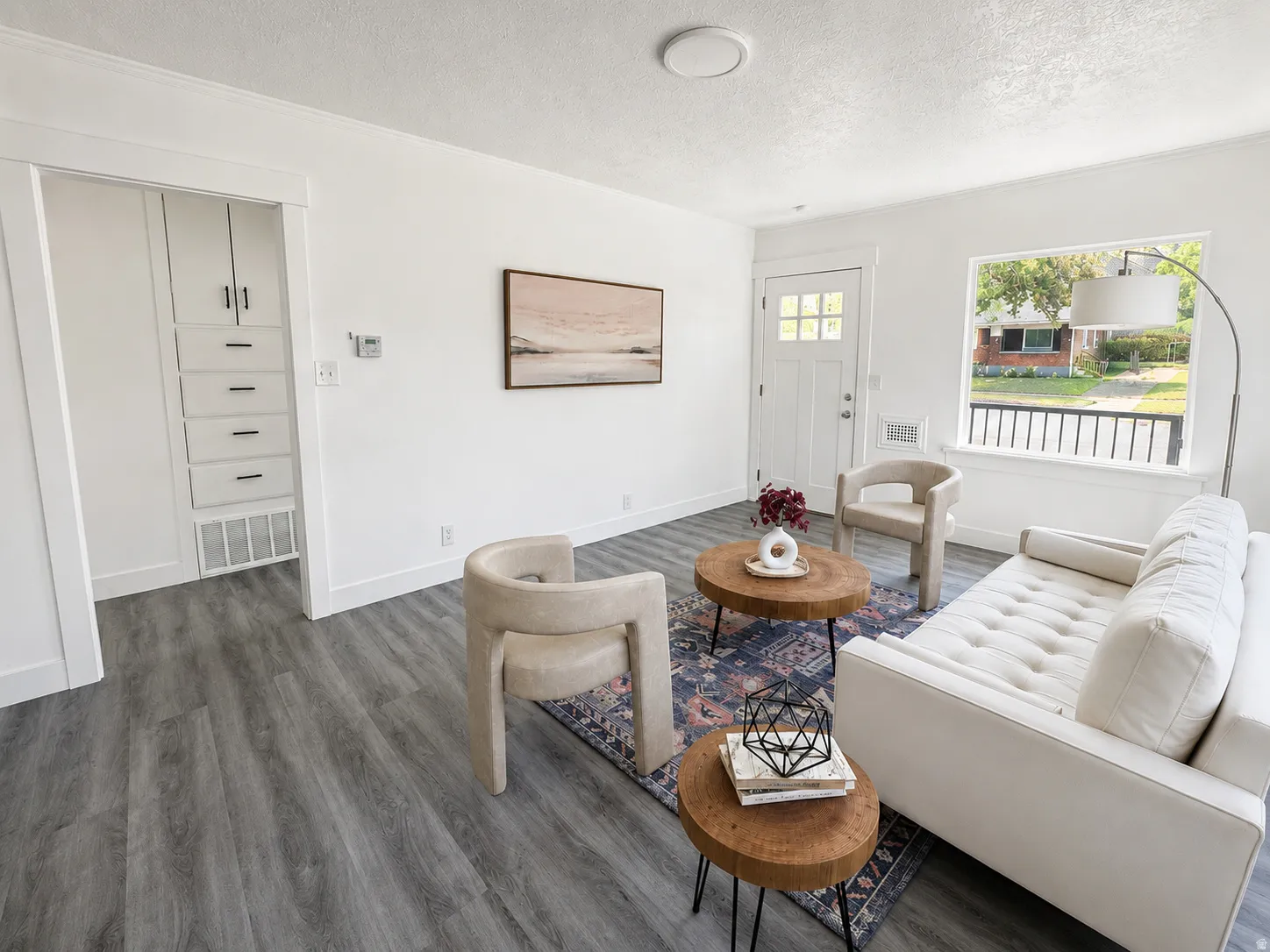 Spacious living area featuring contemporary gray wood-finish flooring, white trim, and a built-in storage cabinet with matte black hardware