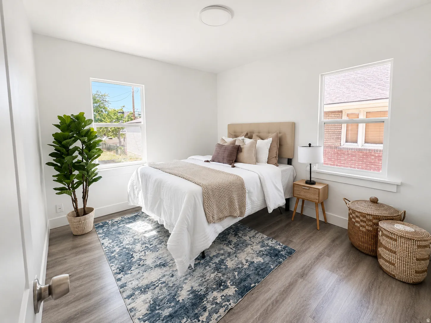 Bright bedroom featuring white walls, wood-finish flooring, and two large windows