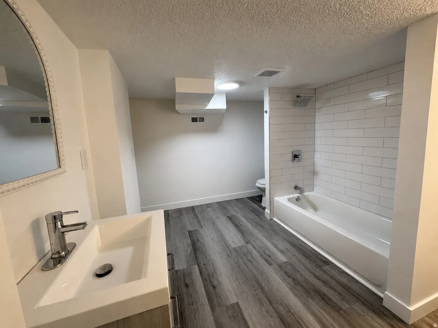 Contemporary bathroom featuring wood-finish flooring and a white subway tile bath surround