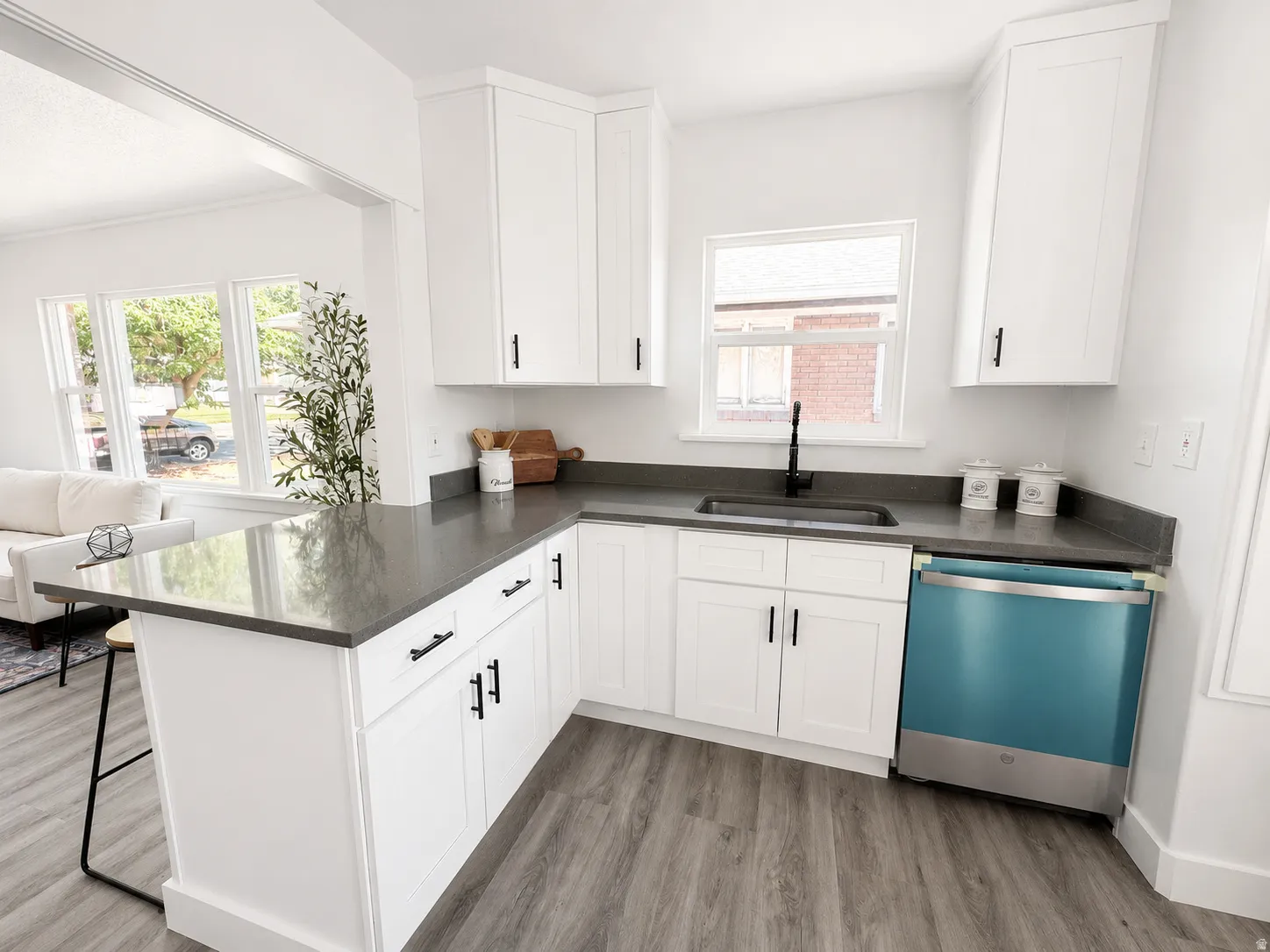 Modern kitchen featuring white shaker cabinetry with matte black hardware, gray countertops, and wood-finish flooring