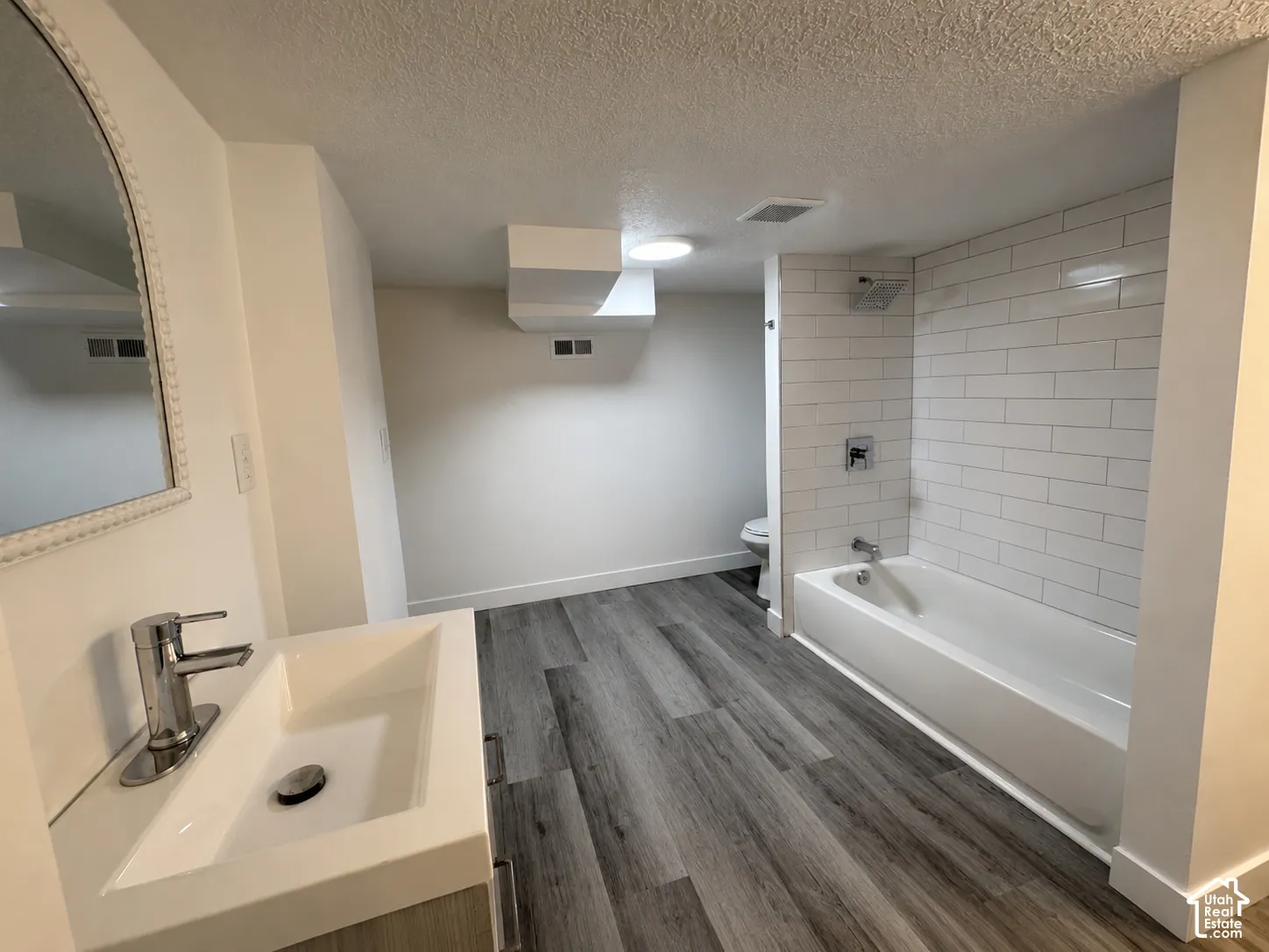 Contemporary bathroom featuring wood-finish flooring and a white subway tile bath surround