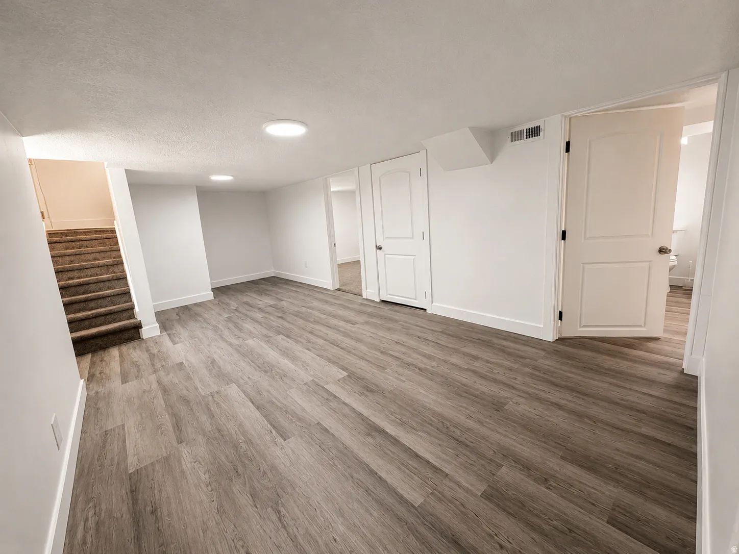 Spacious room featuring wood-finish flooring, white walls with matching baseboards, and bright ceiling lighting