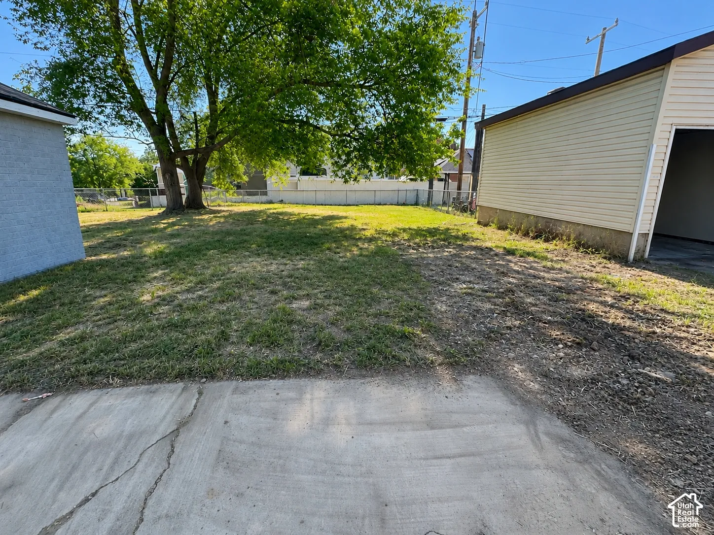 Expansive yard space featuring a mature tree, concrete pad, and a detached garage with horizontal siding