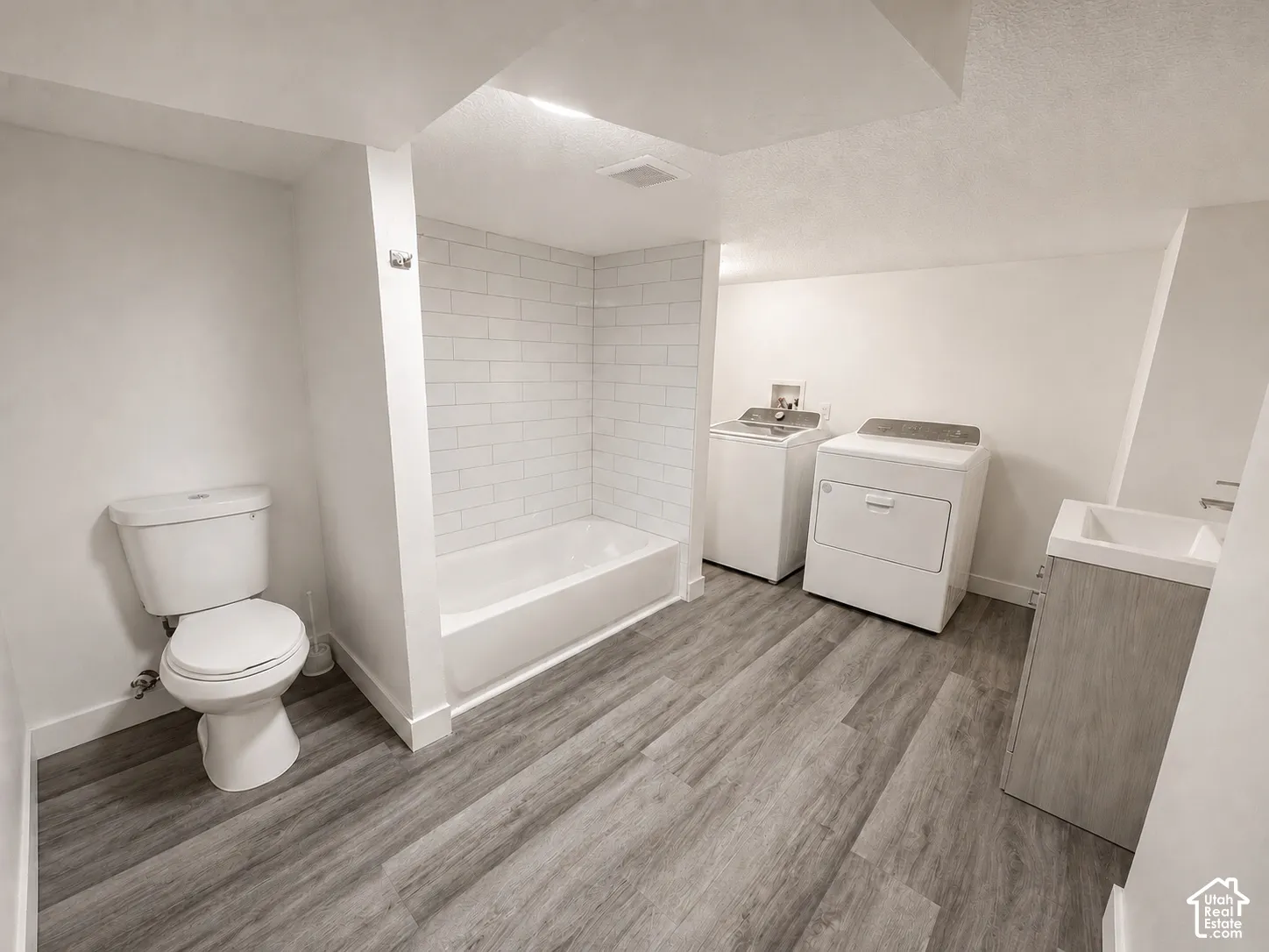Bathroom featuring a white toilet, white bathtub with subway tile surround, and wood-finish flooring