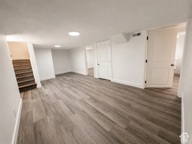 Spacious room featuring wood-finish flooring, white walls with matching baseboards, and bright ceiling lighting