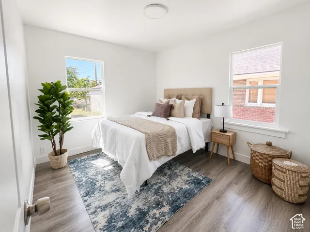 Bright bedroom featuring white walls, wood-finish flooring, and two large windows