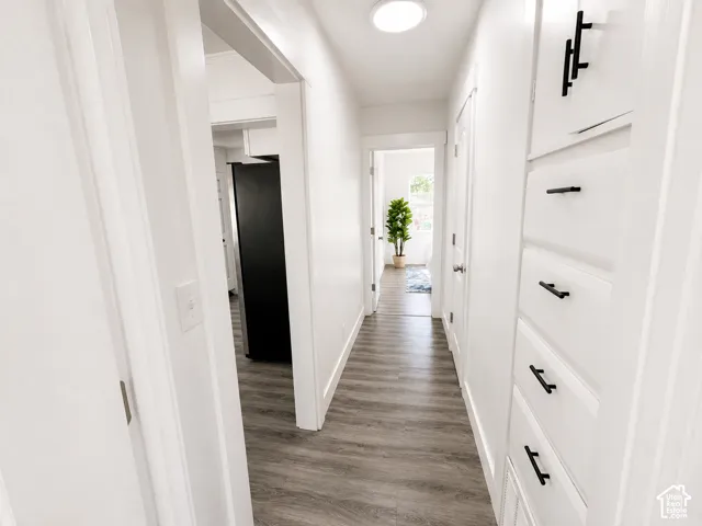 Hallway featuring wood-finish flooring, recessed lighting, white built-in cabinetry with matte black hardware, and crisp white walls