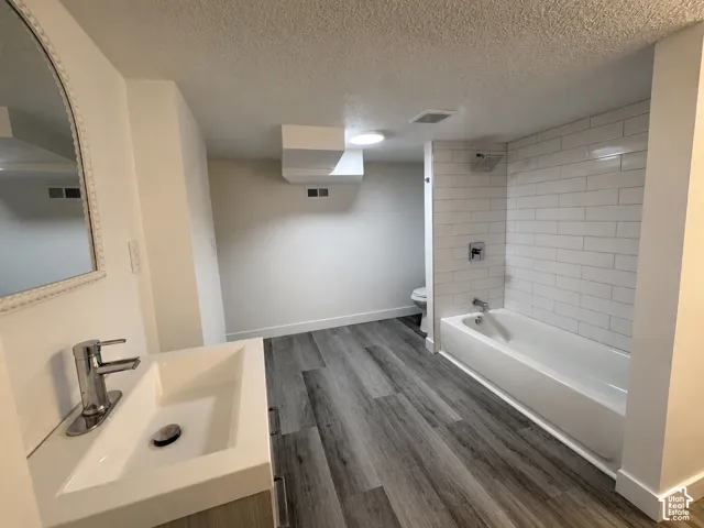 Contemporary bathroom featuring wood-finish flooring and a white subway tile bath surround
